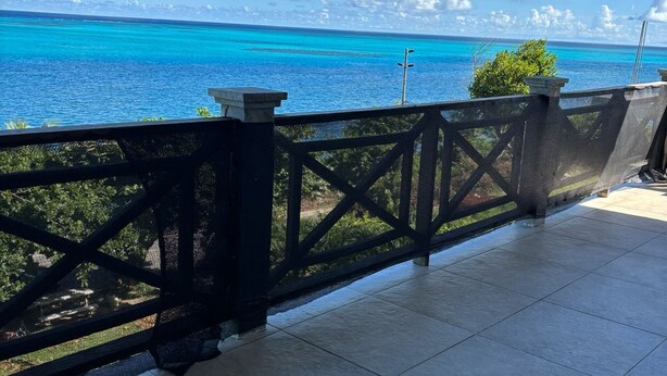 A covered outdoor area with a view of the ocean, a tiled floor, and a black metal railing.