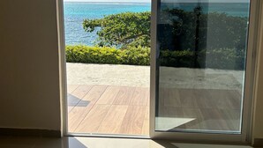 A room with a sliding glass door leading to a balcony with a view of the ocean and a clear sky.