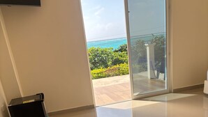A modern room with a large sliding glass door leading to a balcony with a view of the ocean.