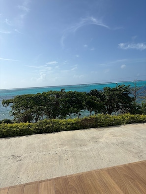 A concrete deck with a wooden floor, overlooking a turquoise sea and dense greenery.