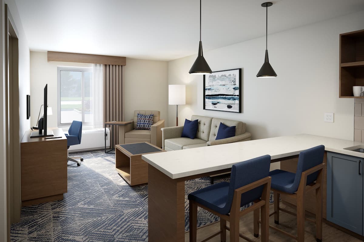 A modern hotel room with a dining area, a sofa, a desk, and a view of the outdoors.