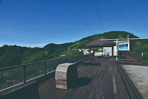 A wooden deck with a bench, a covered seating area, and a view of a green hill. - Intercontinental Taipei by IHG (Taipei)