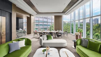 A modern living room with green sofas, a marble coffee table, and a dining area with a view of a cityscape through large windows.