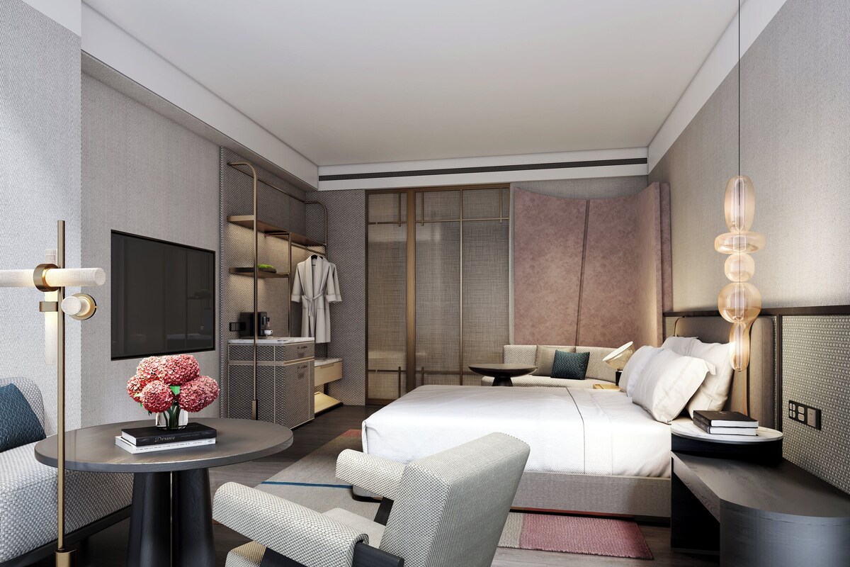 A modern hotel room with a bed, seating area, TV, and a minibar.