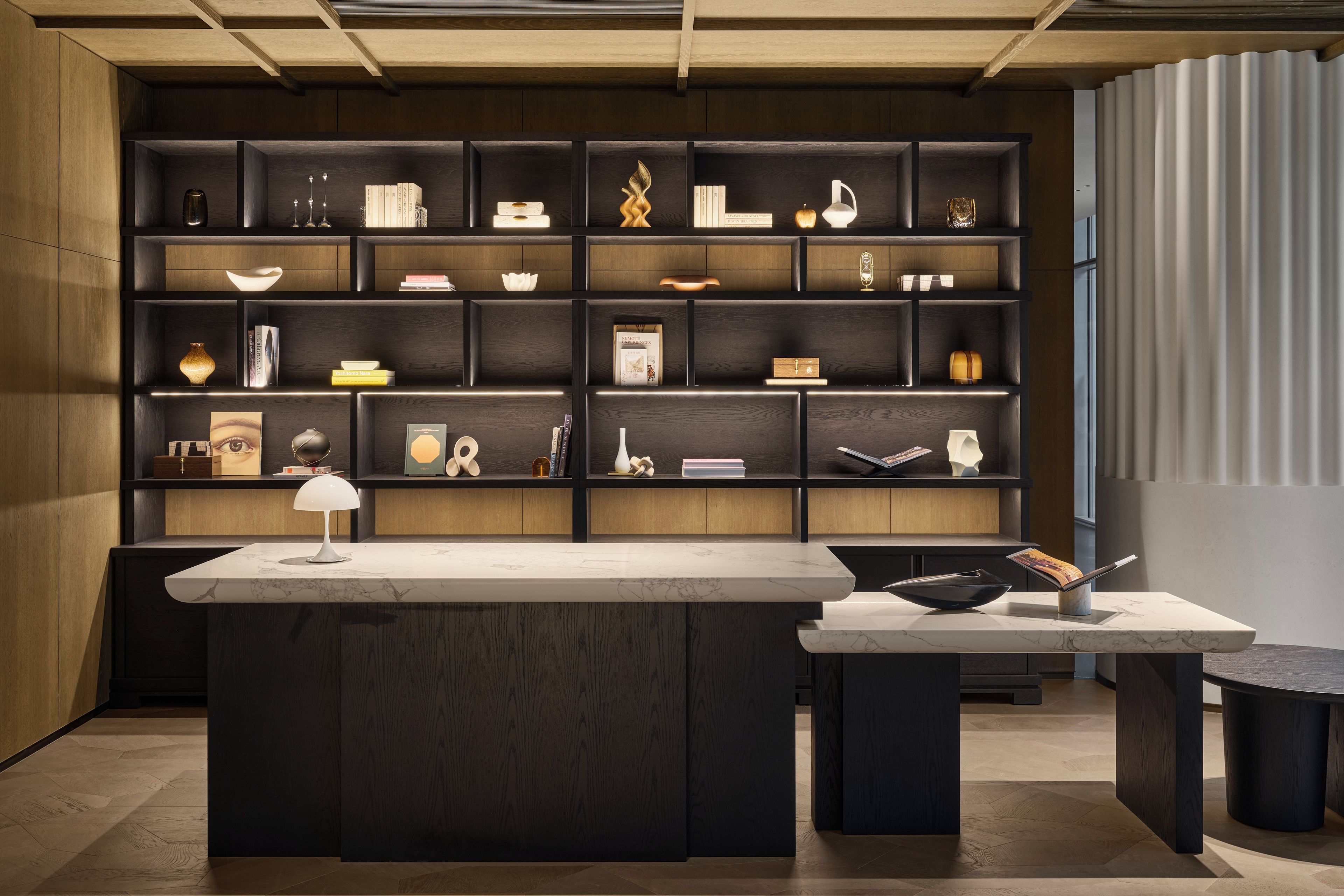 Un interior moderno con una isla central y múltiples estantes llenos de libros y objetos decorativos.