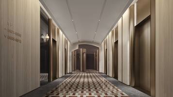 A long, narrow hallway with a patterned floor, wooden walls, and a ceiling with recessed lighting.