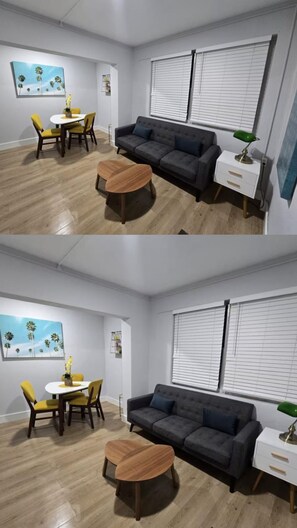 Ein modernes Wohnzimmer mit einem dunkelgrauen Sofa, einem runden Holztisch, einem weißen Beistelltisch mit einer grünen Lampe und einem Palmen-Gemälde an der Wand.