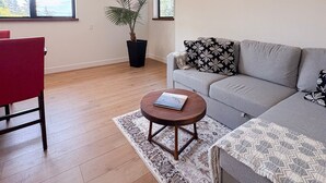 A modern living room with a grey sofa, a red chair, a round wooden coffee table, a patterned rug, and a large window with a view of trees.