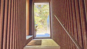 A narrow, wooden interior corridor leading to a door with a view of greenery outside.
