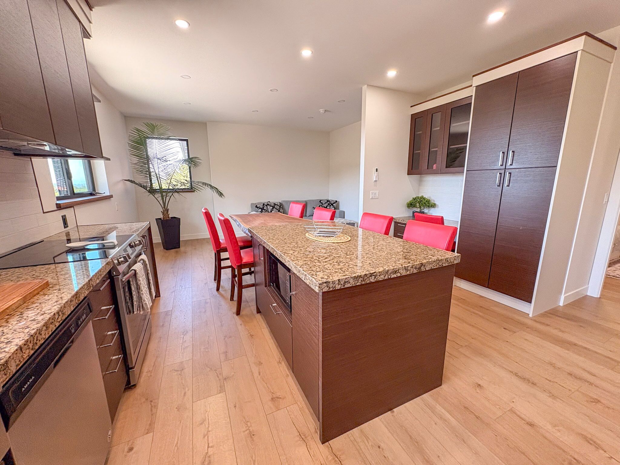A modern kitchen with granite countertops, red chairs, and wooden cabinets.