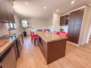A modern kitchen with granite countertops, red chairs, and wooden cabinets.