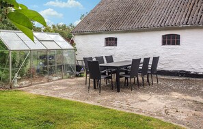 A greenhouse with a glass structure, a white building with a tiled roof, and a table with chairs in the foreground. - 3 bedroom lovely home in Løkken (Løkken)