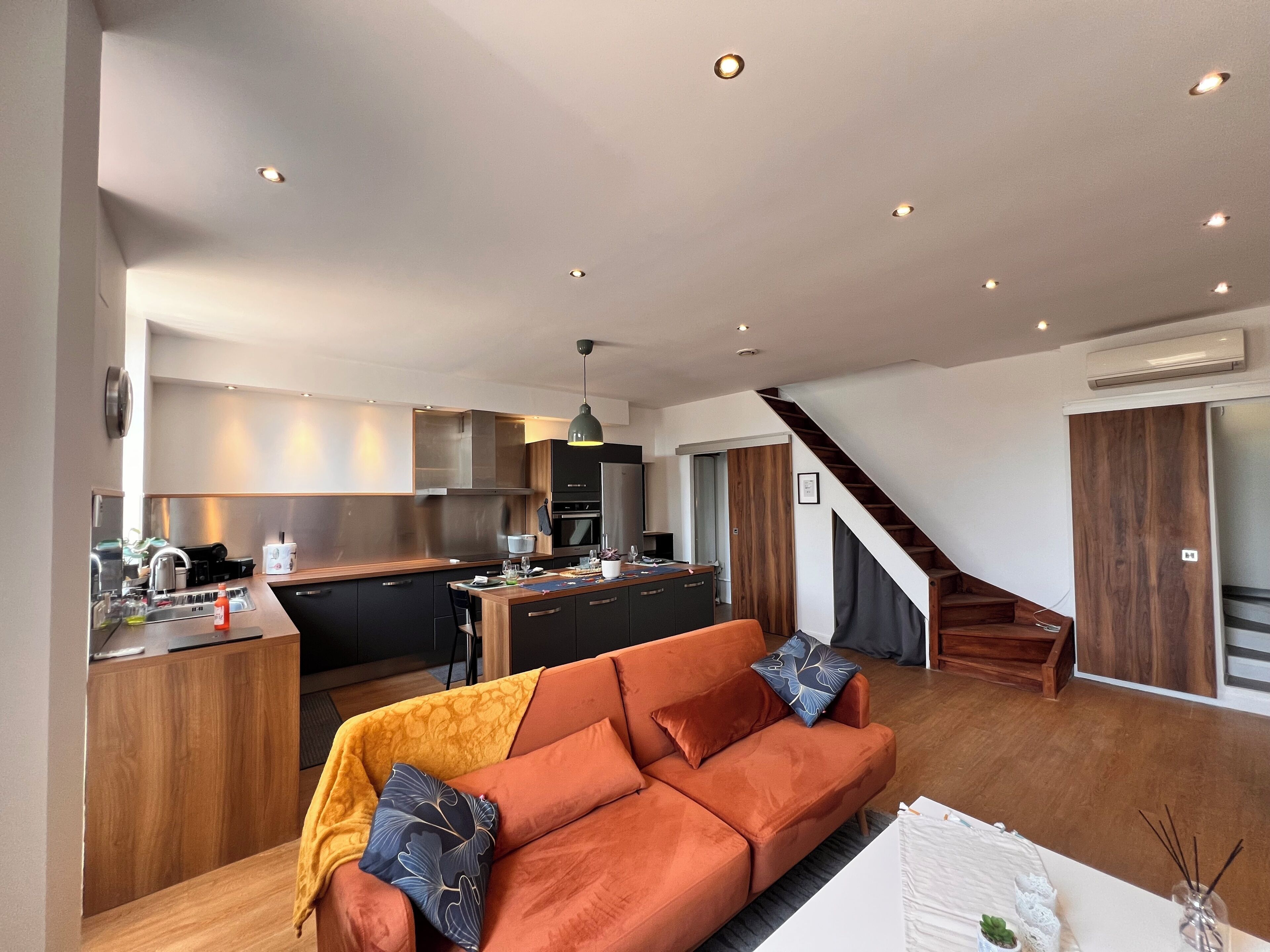 Une cuisine moderne avec un îlot central, un canapé agrémenté de coussins et un escalier menant à un autre niveau.