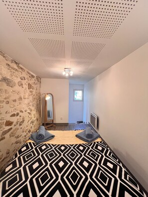 A bedroom with a patterned bedspread, a stone wall, a mirror, and a ceiling with a light fixture. - Charming, air-conditioned house near the highway and public transportation (Marseille)