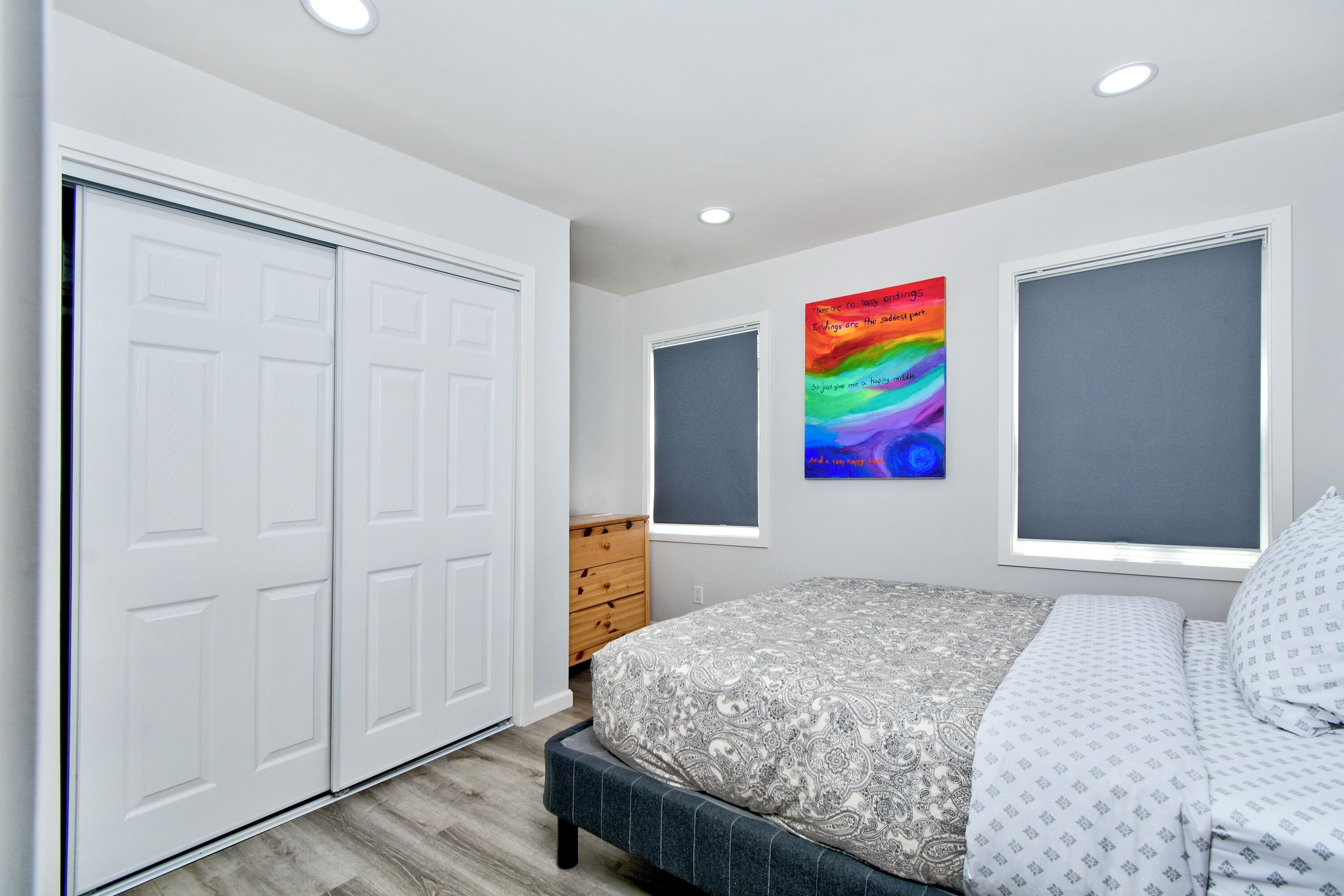 A bedroom with a bed, a wardrobe, a dresser, and a colorful abstract painting on the wall.