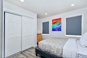 A bedroom with a bed, a wardrobe, a dresser, and a colorful abstract painting on the wall.