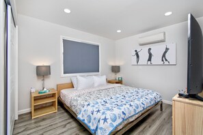 Un dormitorio con cama, mesitas de noche, televisión y una obra de arte en la pared.