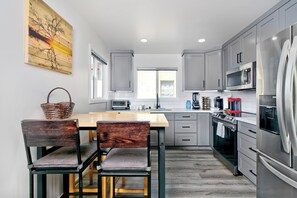 Une cuisine moderne avec des meubles gris, un réfrigérateur en acier inoxydable, un four à micro-ondes et une table à manger en bois avec des chaises.