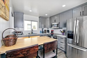 Una cocina moderna con armarios grises, un refrigerador de acero inoxidable, un microondas y una mesa de comedor de madera con sillas.