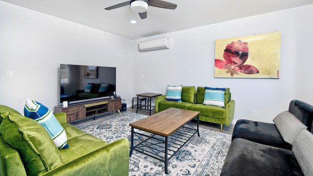 Een moderne woonkamer met een flatscreen-televisie, groene banken, een houten salontafel en een plafondventilator.