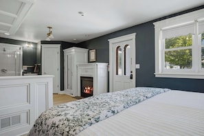 Un dormitorio con chimenea, una cama con ropa de cama floral, un armario blanco y una ventana con vistas.