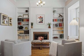 A living room with a fireplace, bookshelves, and a chandelier.