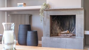 Een haard met houtblokken, een radiator en twee zwarte vazen op een plank.