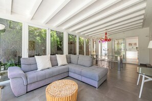 A modern living room with a grey sectional sofa, a round wooden coffee table, and a glass dining table with chairs. - Villa NIKA - Mondello: Exclusive villa located in Fondoanfossi (Palermo)