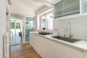 A modern kitchen with a large island, a built-in sink, and a window overlooking a garden. - Villa NIKA - Mondello: Exclusive villa located in Fondoanfossi (Palermo)
