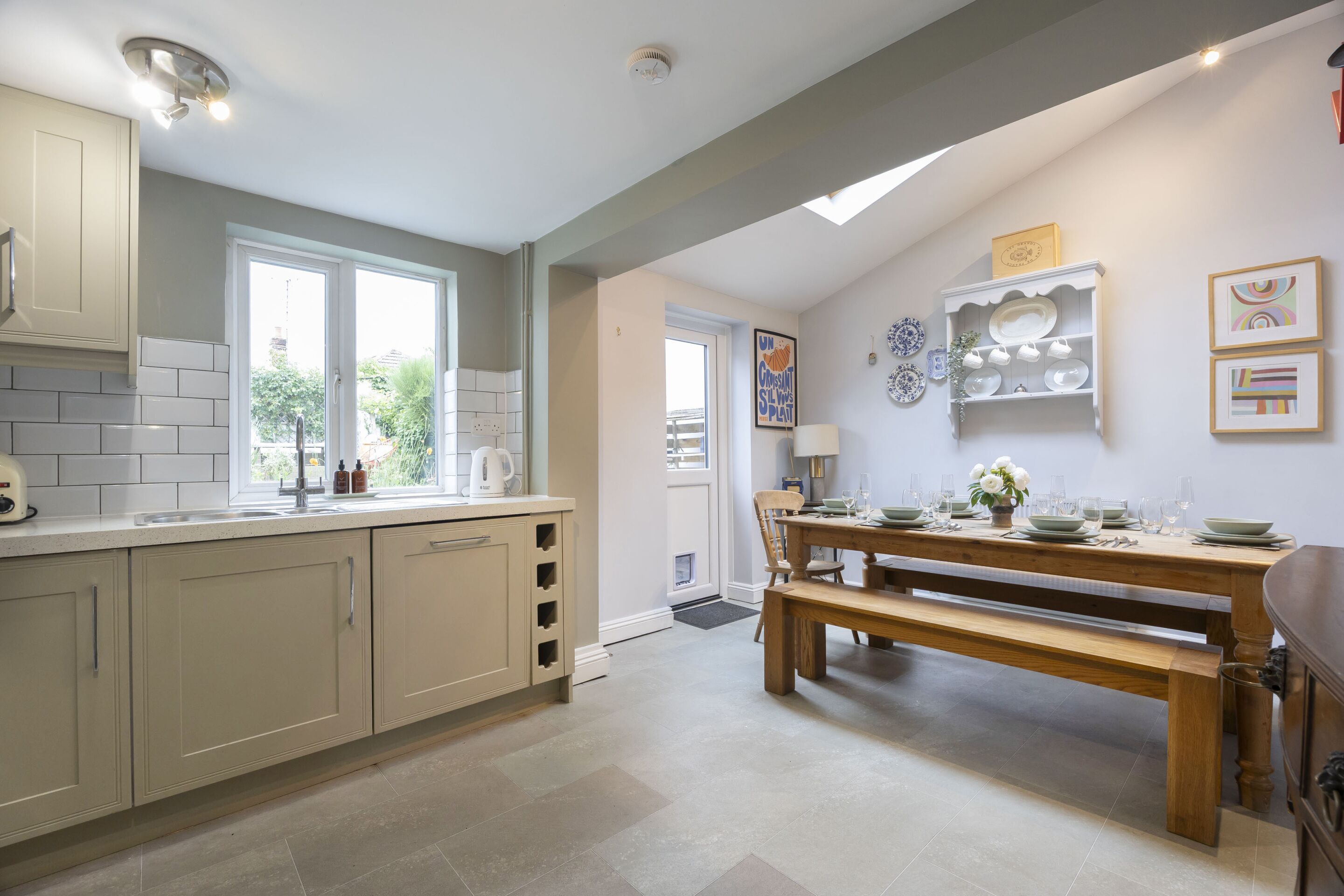 A kitchen with a dining area, featuring a wooden table, a bench, and a window.