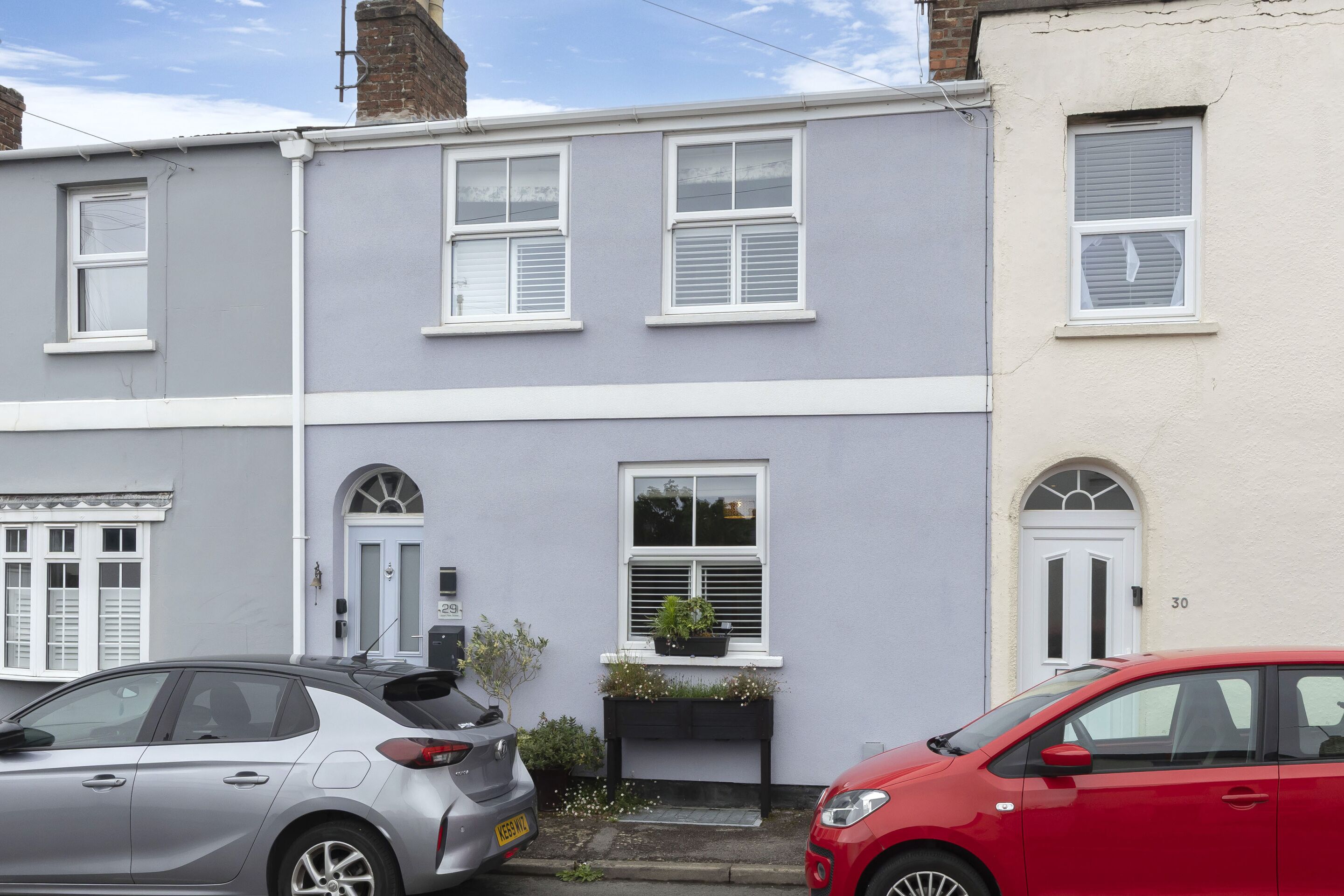 A row of terraced houses with white-framed windows, a small front garden with a planter, and a visible house number.
