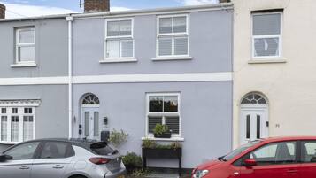 A row of terraced houses with white-framed windows, a small front garden with a planter, and a visible house number.