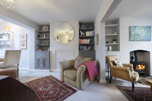 A cozy living room with a fireplace, a round mirror, and a bookshelf. - Charming 3-Bedroom Home with Cosy Log Burner (Cheltenham)