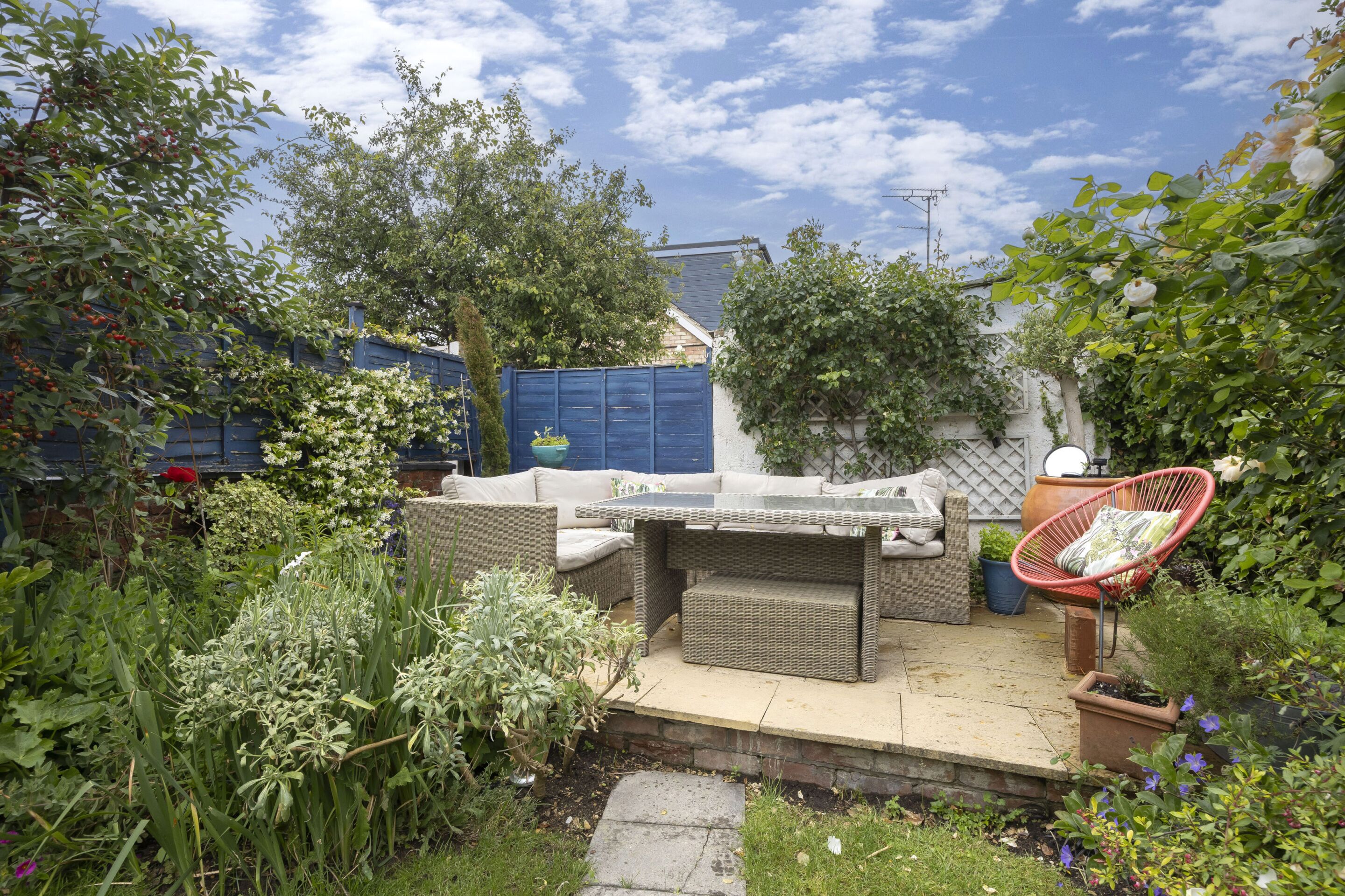 Eine Terrasse mit Korbmöbeln, einem roten Stuhl und Topfpflanzen.