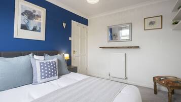 A bedroom with a bed, a nightstand, a lamp, a framed picture, a mirror, and a small wooden table.