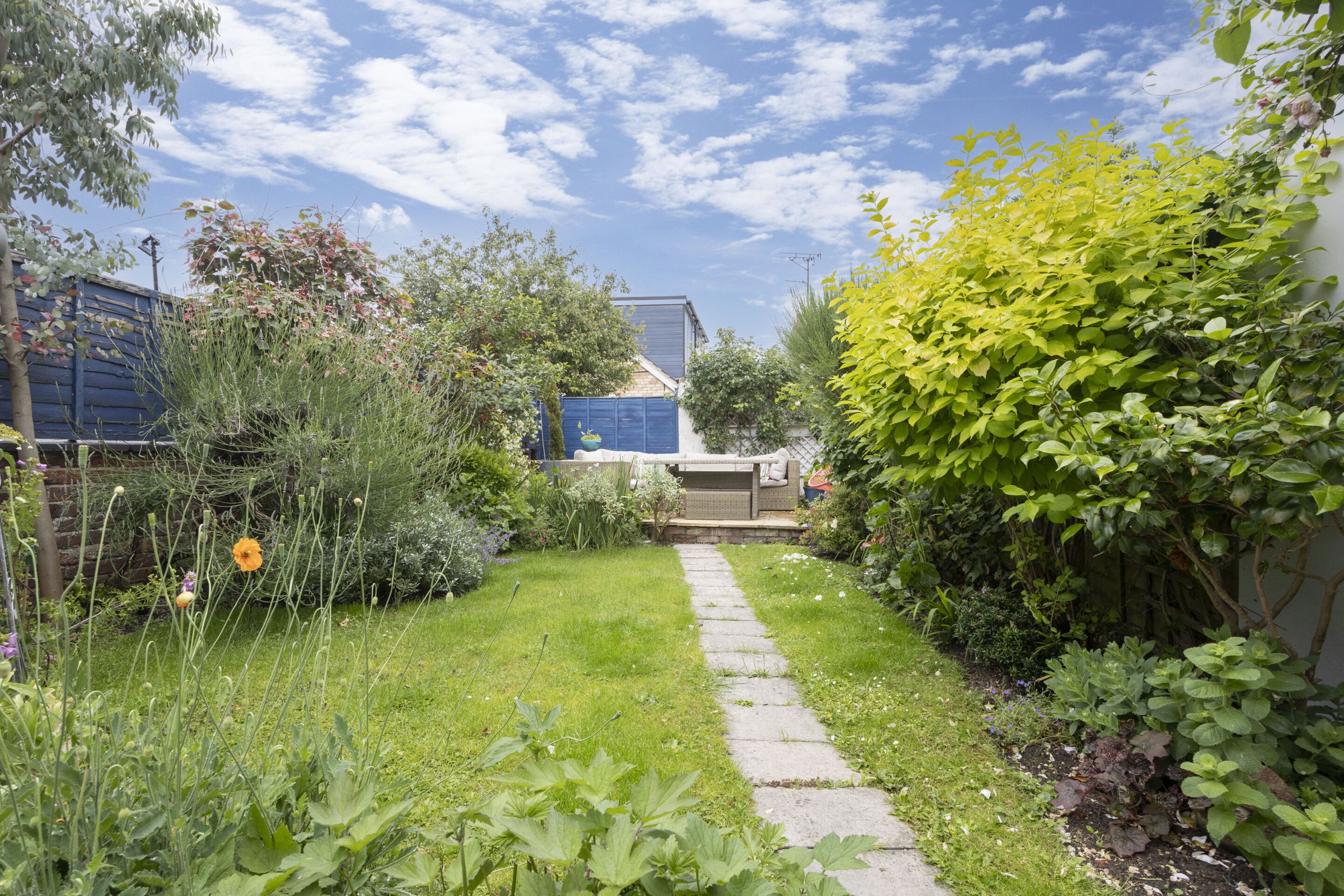 Ein Gartenweg, der zu einem Gebäude mit einer überdachten Außenbestuhlung führt.
