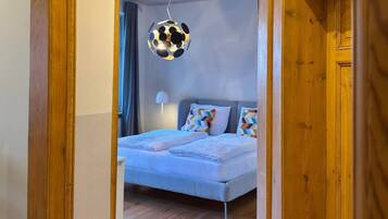 A bedroom with a bed, a hanging light fixture, and wooden flooring.