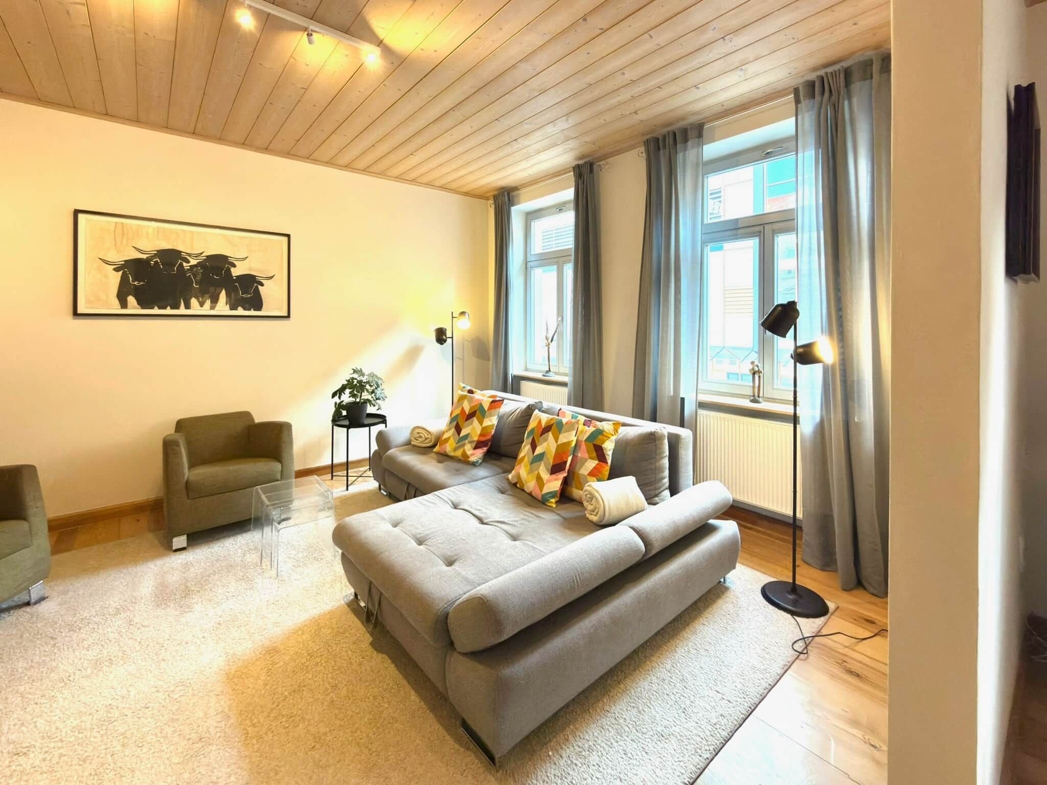 A modern living room with a grey sofa, a small armchair, a floor lamp, and a painting on the wall.