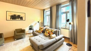 Ein modernes Wohnzimmer mit einem grauen Sofa, einem kleinen Sessel, einer Stehlampe und einem Bild an der Wand.