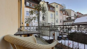 Ein Balkon mit Korbmöbeln, einem Metallgeländer und Blick auf benachbarte Gebäude.