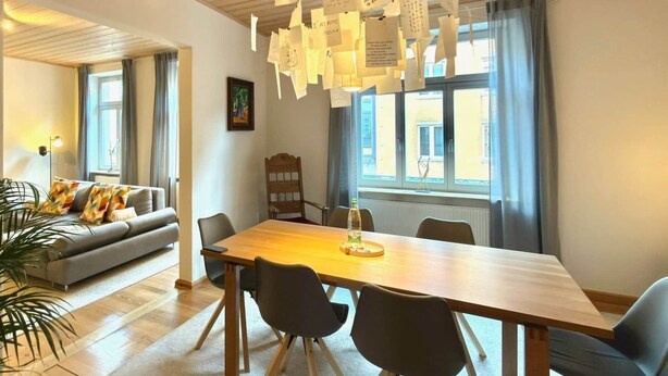 Ein moderner Essbereich mit einem Holztisch, schwarzen Stühlen und einer hängenden Leuchte.