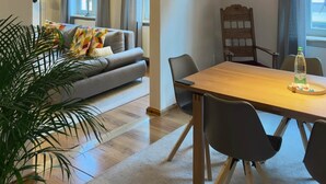 Ein modernes Wohnzimmer mit Holzboden, einem Esstisch mit Stühlen, einer Couch und einer großen Topfpflanze.