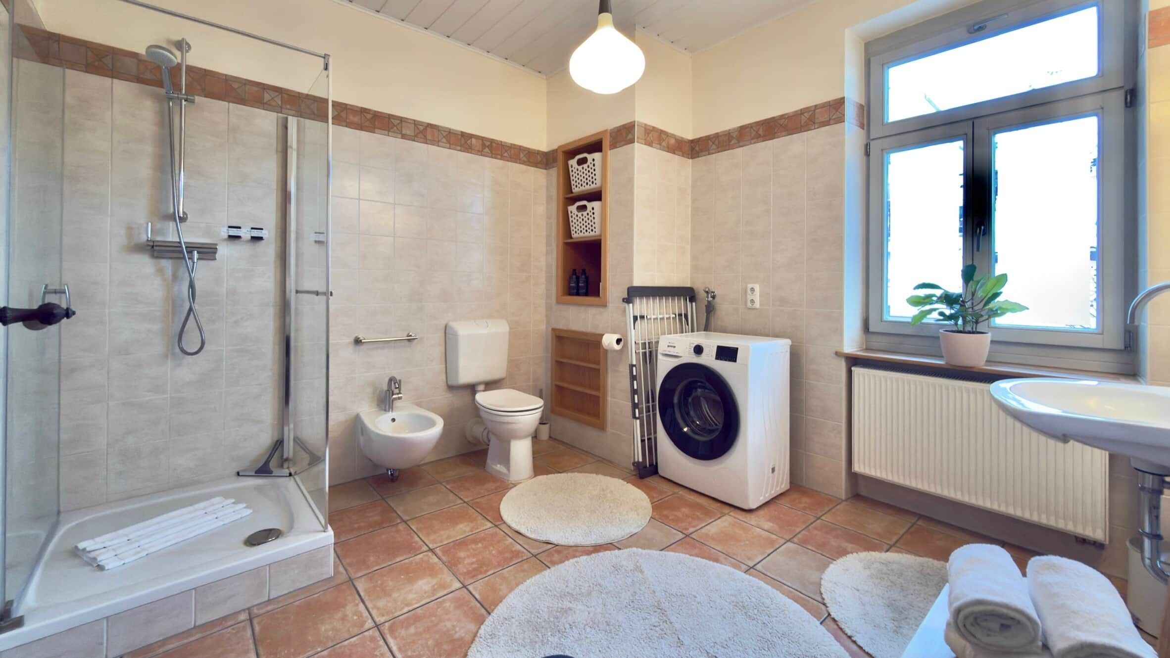 A bathroom with a shower, toilet, washing machine, and sink.