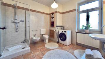 A bathroom with a shower, toilet, washing machine, and sink.
