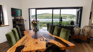 Un tavolo da pranzo con sedie, un vaso con fiori e vista su un lago attraverso ampie finestre.