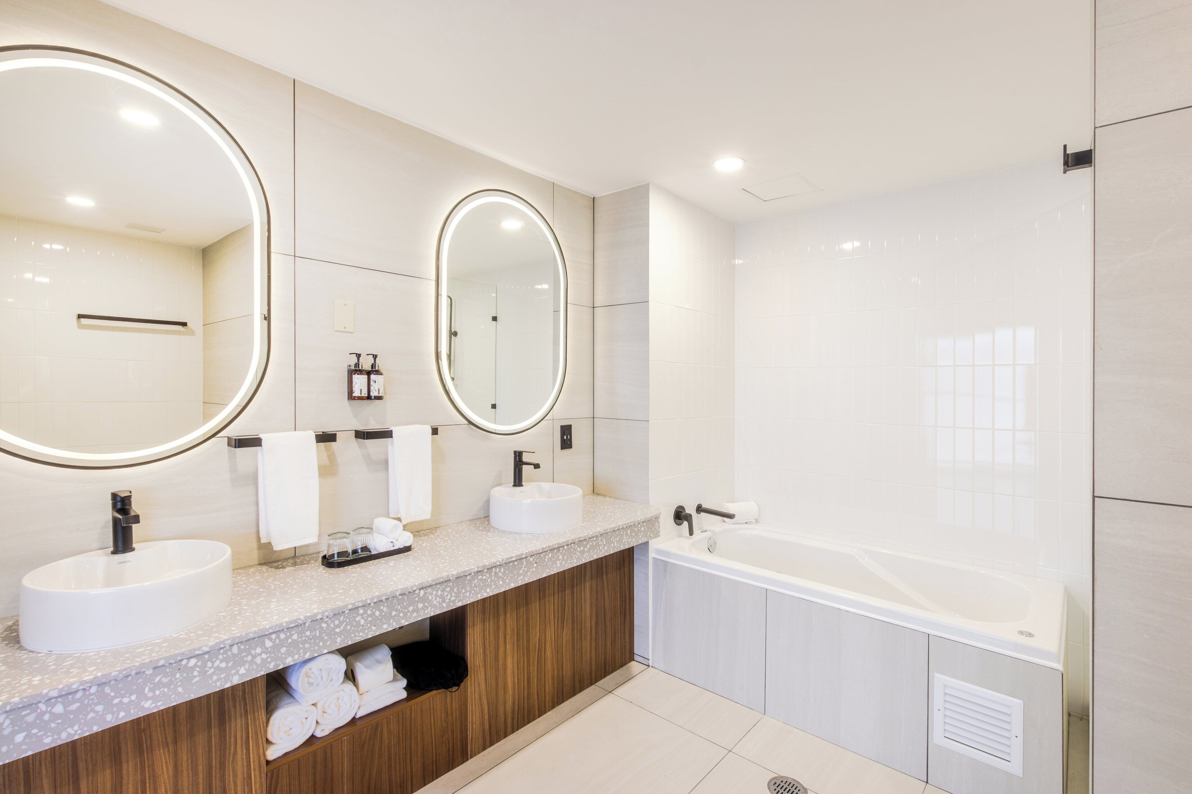 Un baño moderno con dos lavamanos, un espejo grande y una bañera.