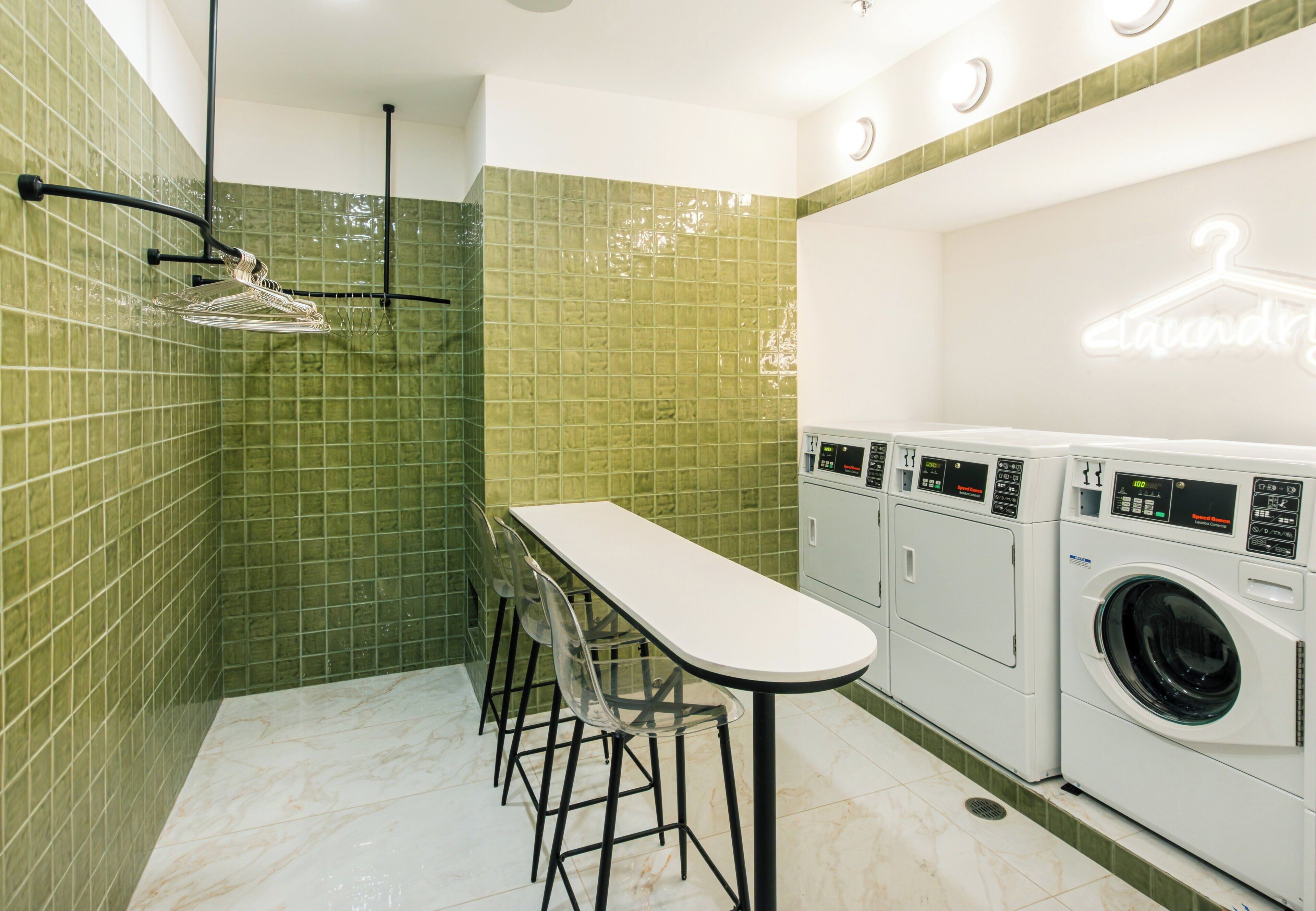 A compact laundry room with a white table and chairs, a drying rack, and a row of washing machines.
