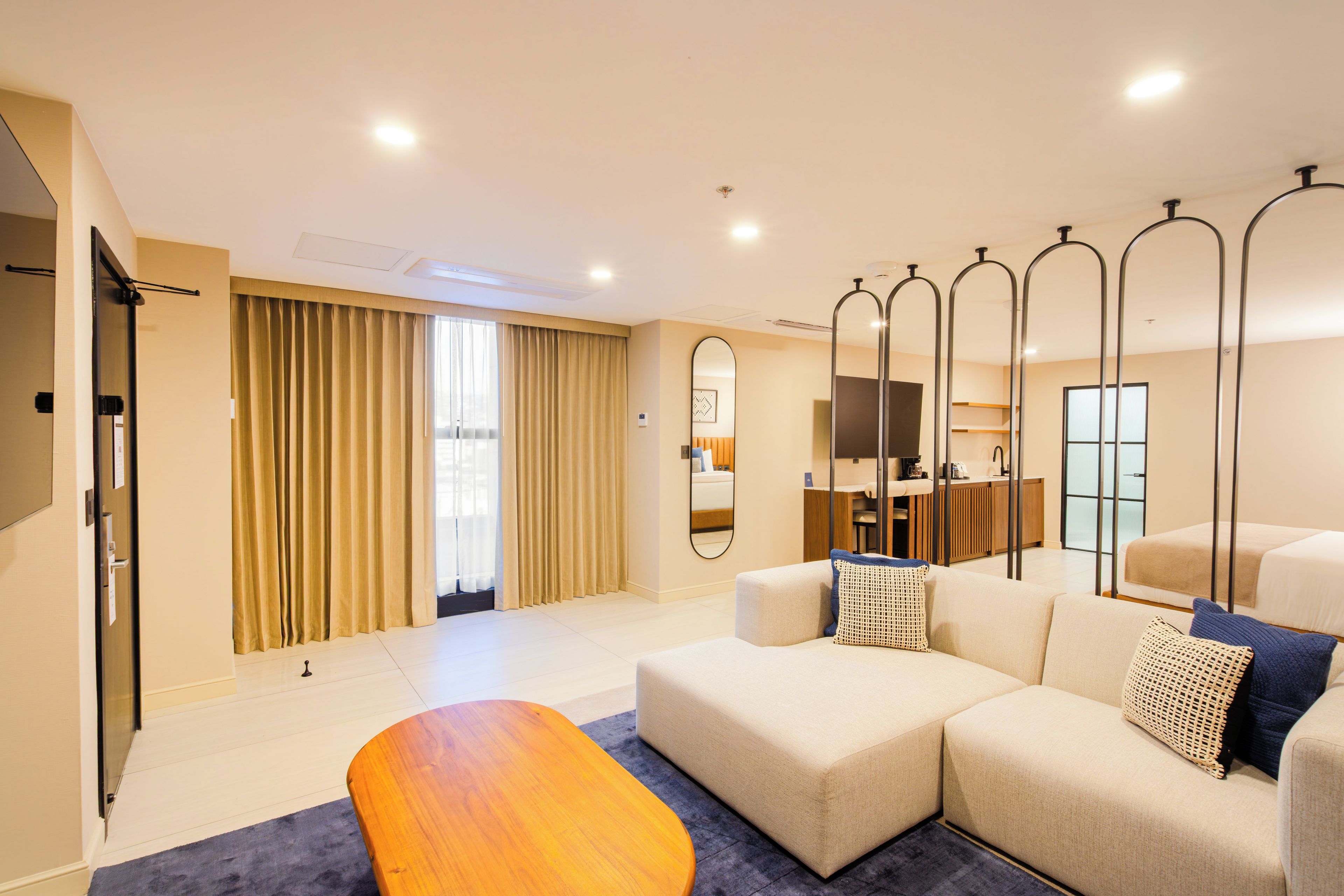 A modern hotel room with a sofa, a wooden coffee table, and a large mirror.