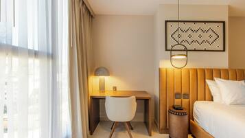 A hotel room with a bed, a desk, a chair, a lamp, and a wall-mounted artwork.