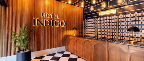 A reception area with a checkered floor, a wooden wall with the text 'HOTEL INDIGO,' and a 'BIENVENIDOS' sign.